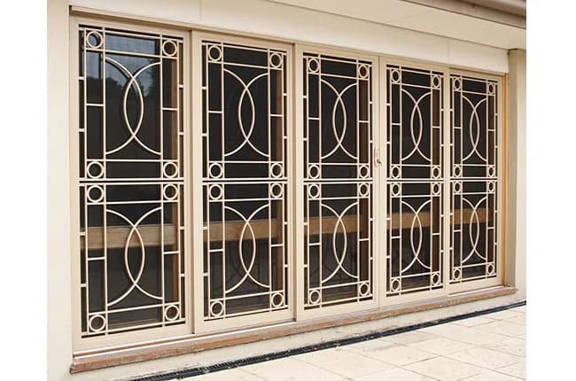 Five cream cast aluminium decorative security screens across a wide patio door opening