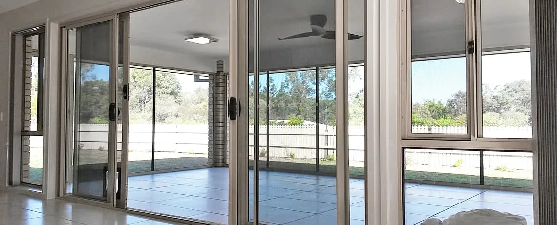 Interior of a home looking out through a wall of sliding doors and windows fitted with security screens